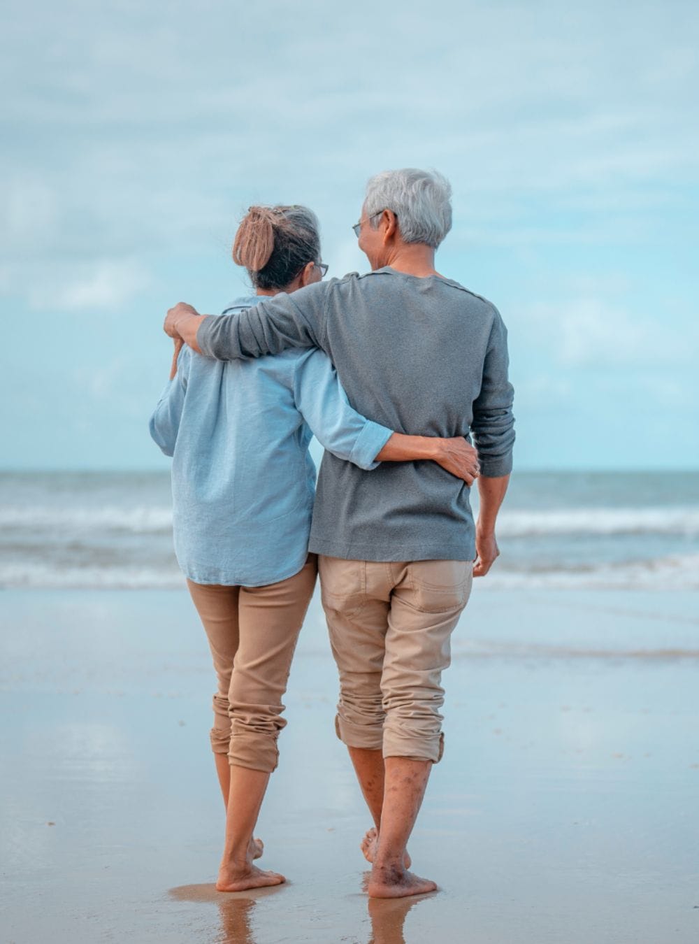 An elderly couple walking along the beach.