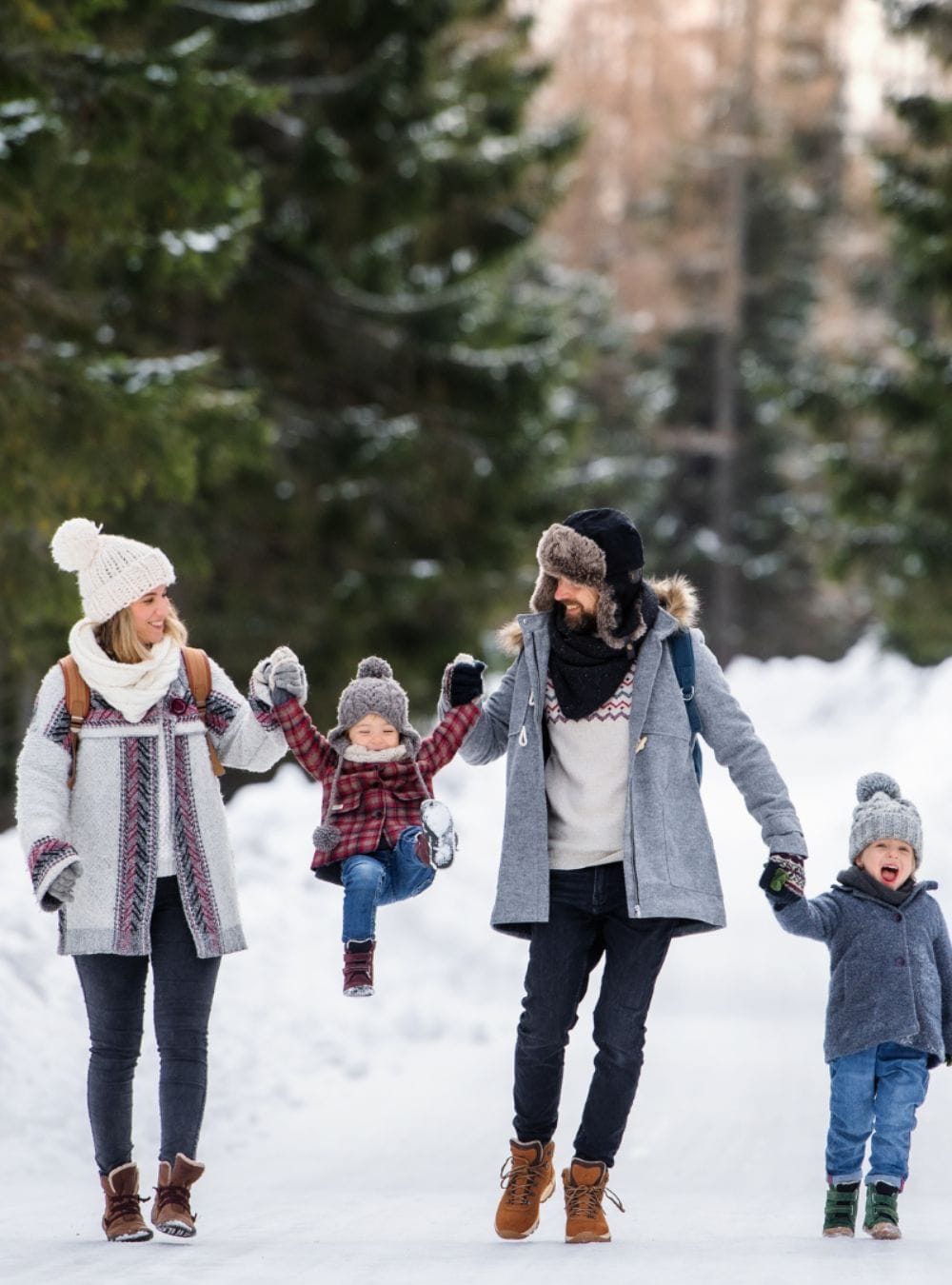 A family with two toddlers playing in the snow and laughing.