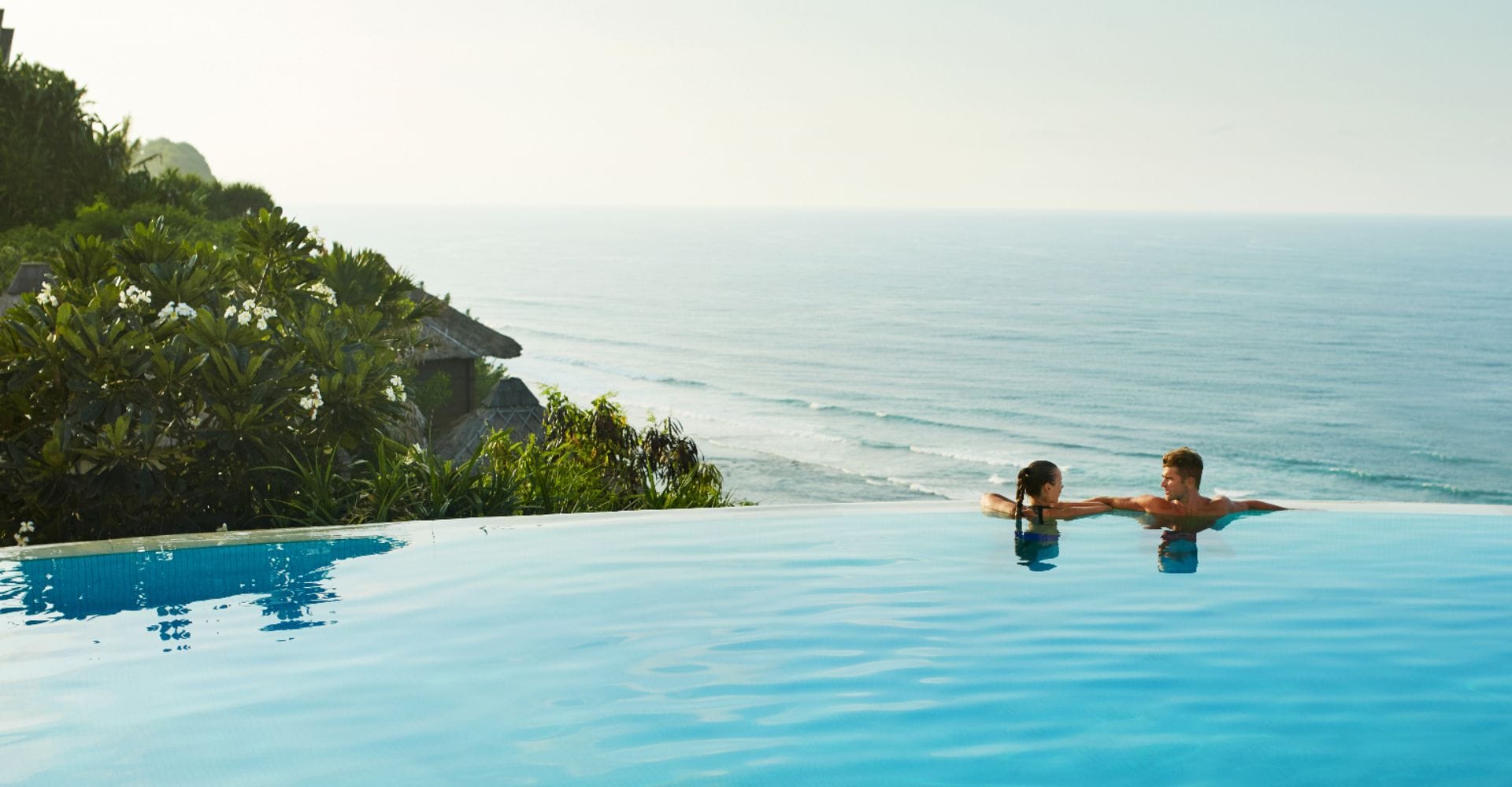 Two people in the pool overlooking the ocean.